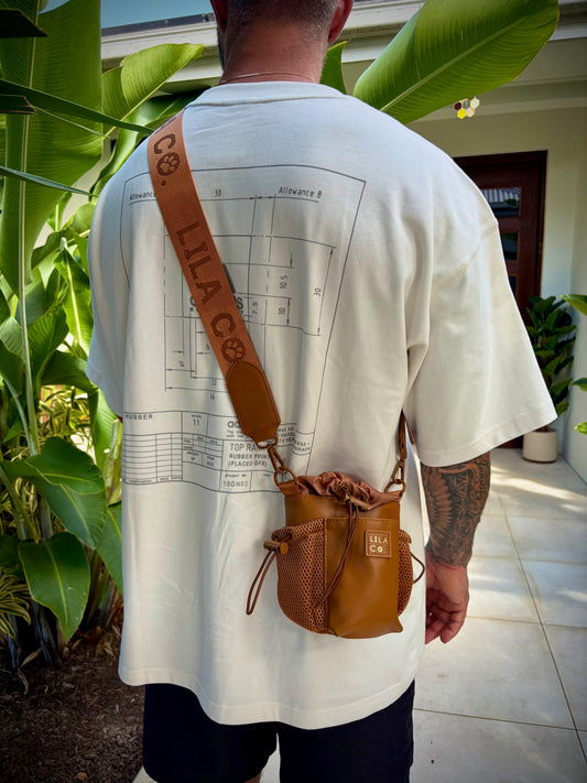 Person wearing a white t-shirt with a graphic design and carrying a brown leather bag outdoors.
