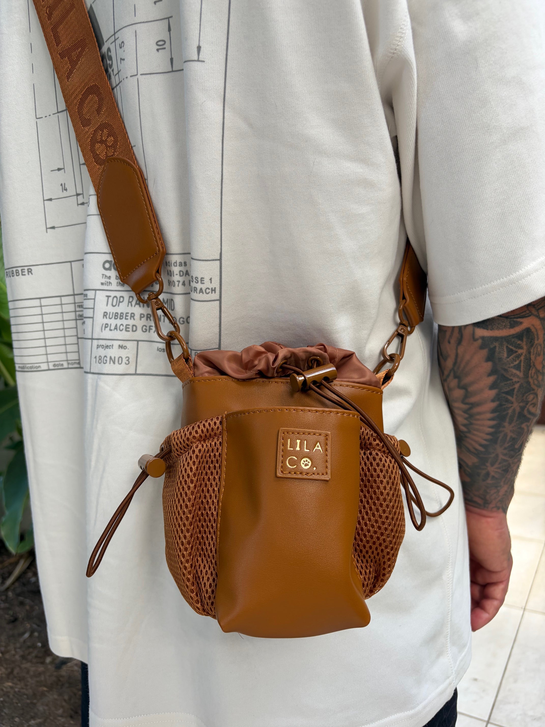 Brown leather pouch with drawstring held by a person on a white surface with blueprints.