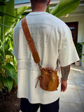 Person wearing a white t-shirt with a graphic design and carrying a brown leather bag outdoors.