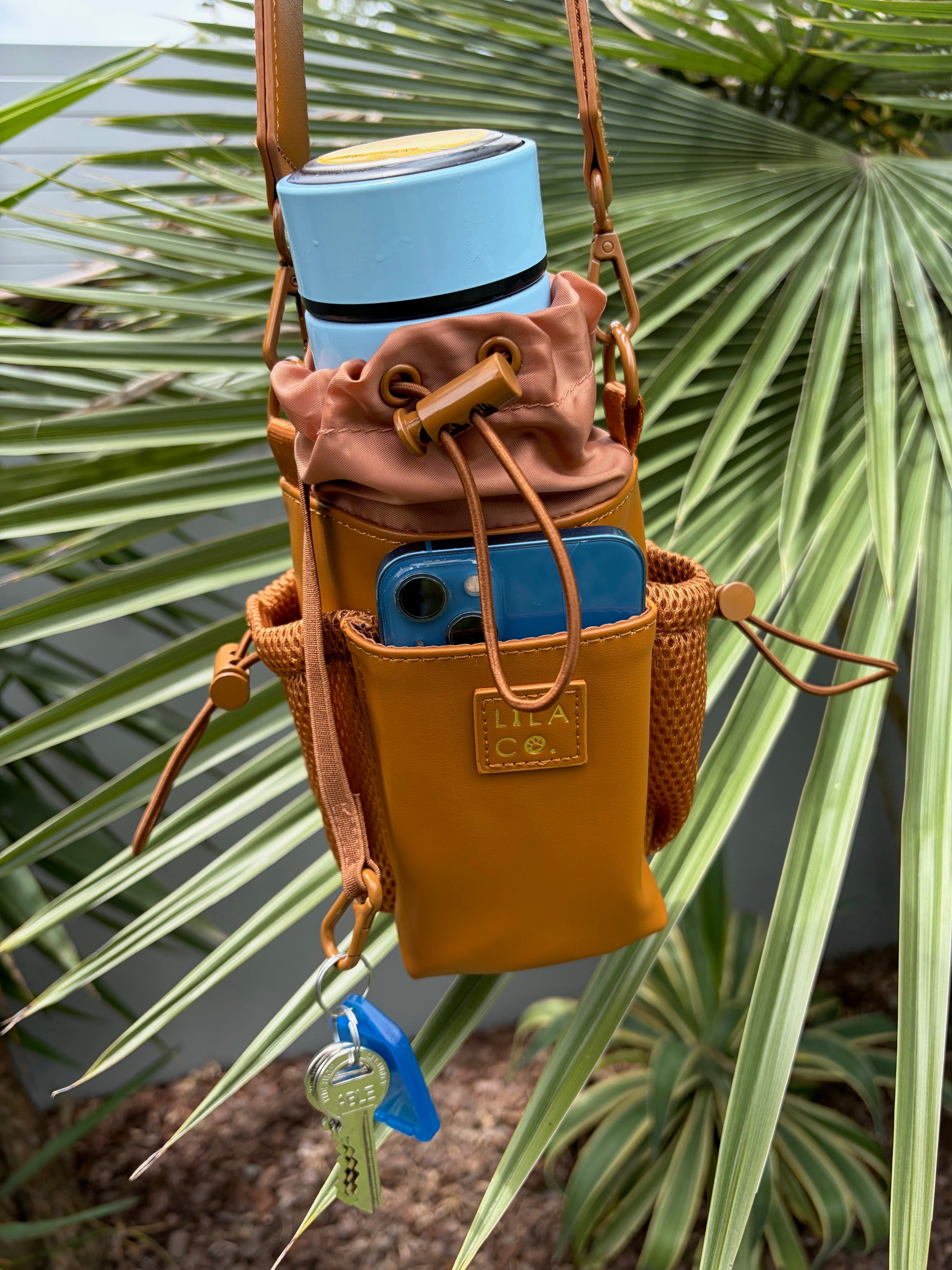 Brown leather crossbody bag with blue accents against a green leafy background